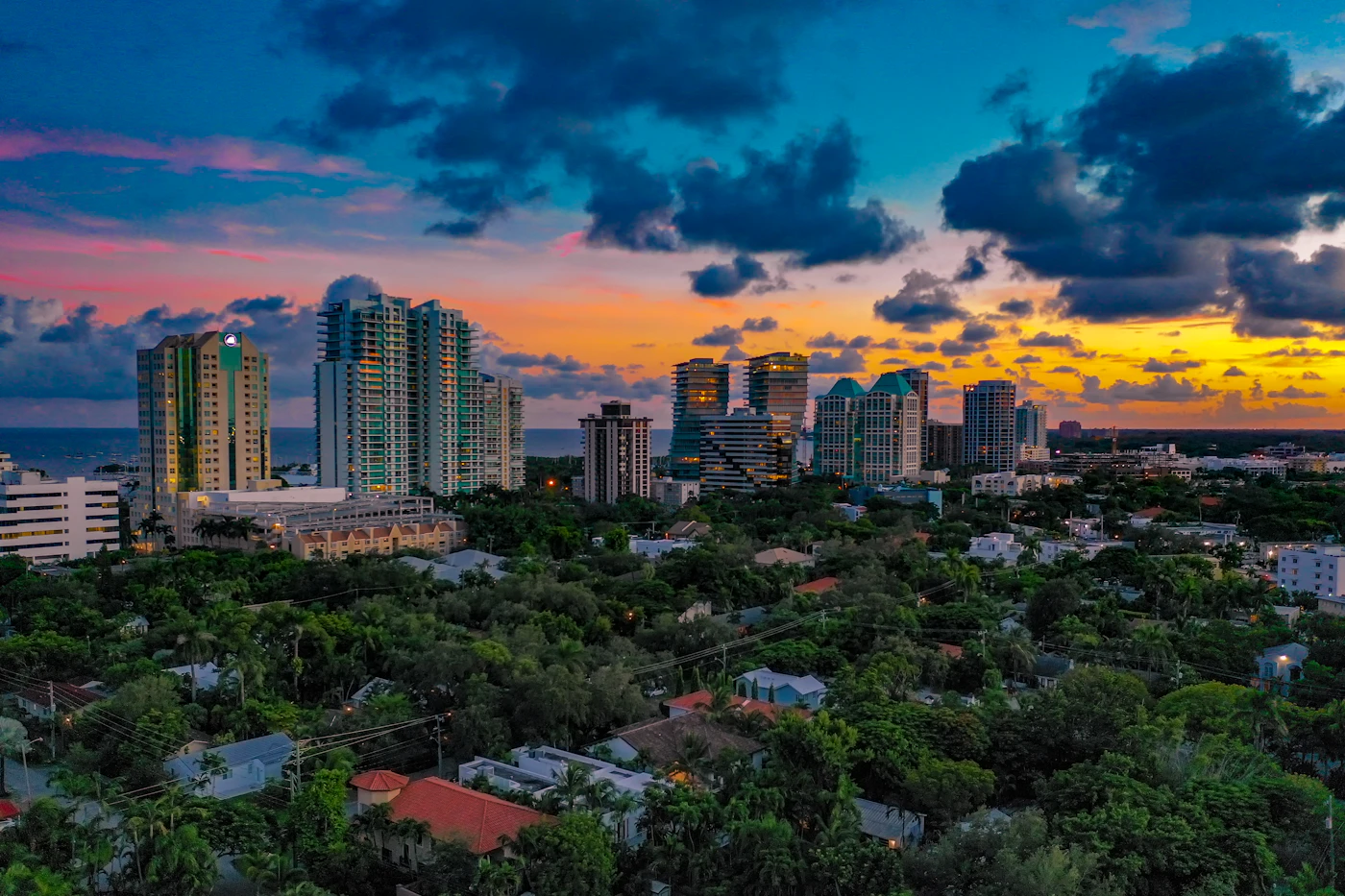 Homes under the tree canopy and the waterfront high-rises of Coconut Grove, Miami, under sunset storm clouds